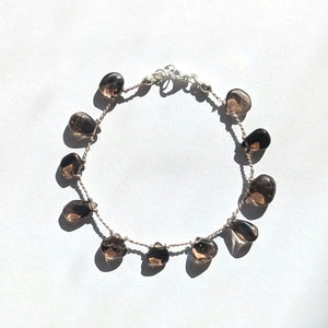 Delicate smokey quartz drop bracelet displayed on a white background, featuring sterling silver and silk cord.